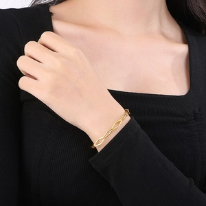 Close-up of gold geometric paperclip chain necklace worn on a black sweater background