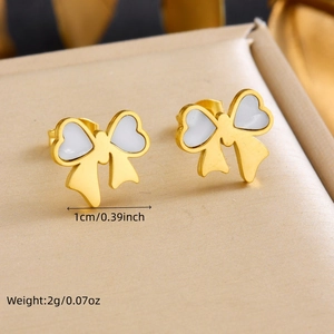 Elegant gold bow stud earrings with white heart enamel on a beige jewelry display