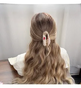 Detail view of a cream hair claw clip with red roses on long wavy brown hair