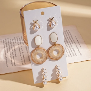 Detailed view of three pairs of gold metal and faux pearl earrings on white card display