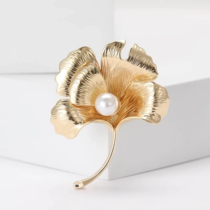 Elegant gold ginkgo leaf brooch with pearl accent on a minimalist white background
