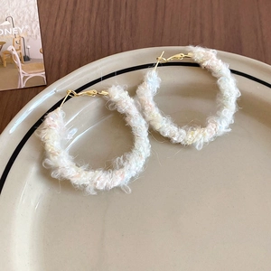 Vue détaillée des boucles d'oreilles rondes en laine blanche tricotée avec fermoir doré sur plat