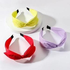 Close-up of fabric knotted headbands in yellow, red, and purple on a white display