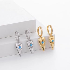 Detail of heart drop earrings with evil eye motifs and blue stones on white steps