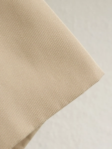 Detailed macro view showing the high-quality twill fabric texture of the beige trench coat