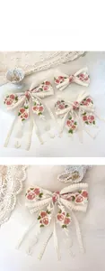 Detailed embroidery of pink roses and green leaves on cream lace bow hair clip