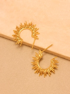 Detailed view of golden sunburst C-shaped earrings on light stone surface