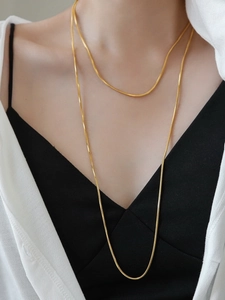 Close-up detail of a minimalist long gold-plated snake bone chain necklace on a model
