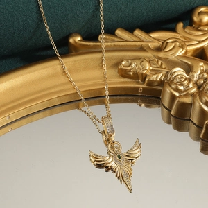 18K gold-plated wing pendant necklace with green gemstone on a vintage mirror