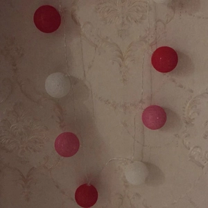 Close-up of cotton ball LED string lights in red, pink and white with woven texture