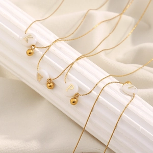 Close-up of four 18K gold plated stainless steel necklaces with letter pendants on marble