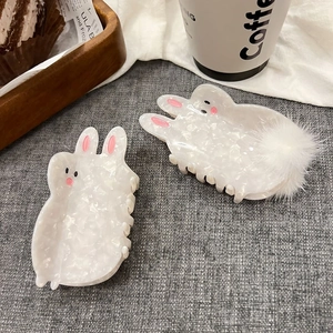 Detail of two cute white rabbit hair claws with pearlescent finish and plush ball detail