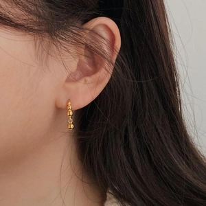 Close-up of a gold-plated C-shaped earring with a dangling bead on a female model