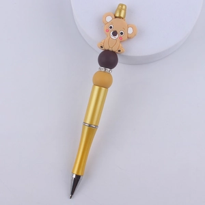 Detail of golden ballpoint pen with cartoon koala topper, colored beads, and rhinestone rings