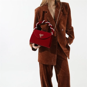 Detail of red velvet handbag with pearl handle and golden bow knot on brown suit