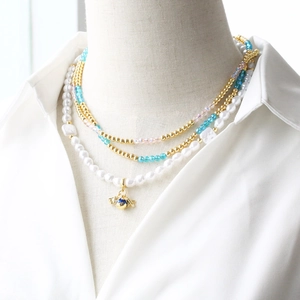 Multilayer beaded necklace with crystal pearls and blue spherical pendant on white shirt
