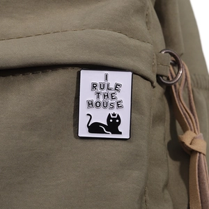 Détail d'un pin's chat noir en émail sur un sac en toile vert montrant la texture du tissu