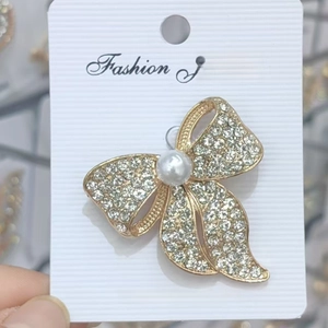 Détail d'une broche en forme de nœud doré avec perles blanches et strass étincelants