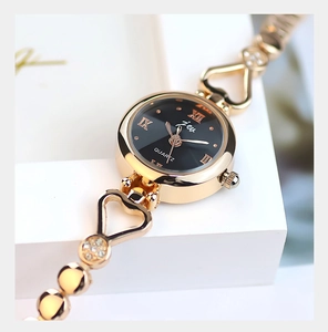 Macro detail of gold ladies quartz watch featuring black dial with crystals and heart chain
