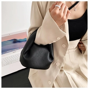 Detail of a black ruched leather cloud bag held by a model in a professional office setting