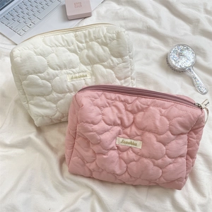 Detail view of quilted cloud texture makeup bags in white and pink with logo patch