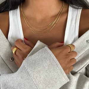 Detailed close-up of 18k gold triple-layer chain necklace and rings on a model