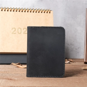 Close-up of black leather card holder with fine hand-stitching on a rustic wooden desk