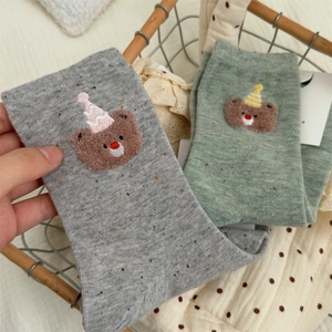 Close-up of cute embroidered bear with party hat on gray and green knit socks