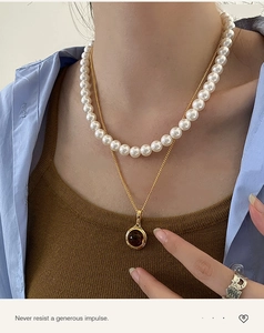 Detail of layered jewelry featuring a pearl necklace and golden pendant on a model