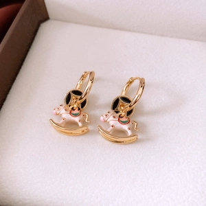 Macro shot of gold-plated rocking horse earrings with white enamel and coin detail