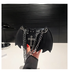 Detail of gothic black bat wing bag featuring silver cross and chunky metal chain strap