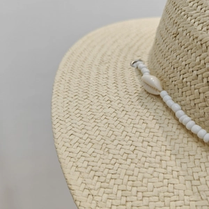 Close-up of woven straw sun hat featuring decorative white beads and natural seashell