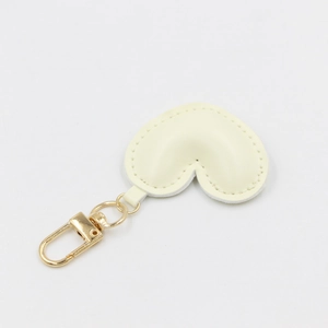 Detail view of a cream heart-shaped PU leather keychain with gold clasp and fine stitching