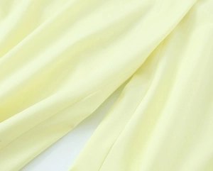 Close-up detail of light yellow plain weave fabric texture and elegant pleated draping