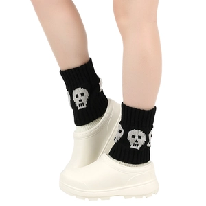 Close-up of black knitted leg warmers with skull patterns paired with white garden clogs
