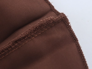 Detail view of high-quality stitching and overlock edge on dark brown pleated fabric