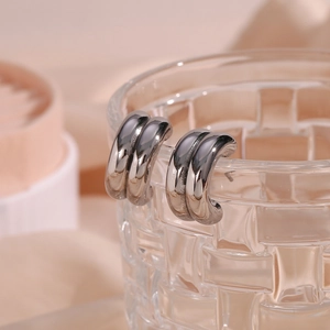 Close-up of silver double-layered ribbed C-shaped earrings on a textured glass rim