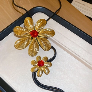 Close-up of golden metal flower pendants with red crystal on a jewelry tray