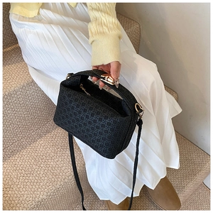 Detail of black woven texture handbag with gold hardware held by model in casual style