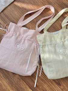 Pink and yellow canvas drawstring tote bags with bow embroidery on wooden floor