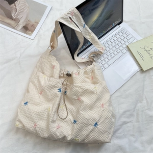 Detail of waffle-textured canvas tote with colorful embroidered bows and drawstring closure