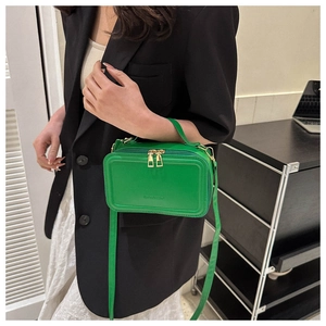 Detail of green suitcase-shaped crossbody bag with gold zipper and fashion text
