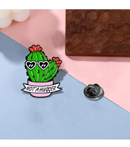 Detail of enamel cactus pin with heart sunglasses and 'NOT A HUGGER' banner text
