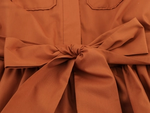 Détail d'une robe en popeline terracotta avec un grand nœud à la taille et surpiqûres