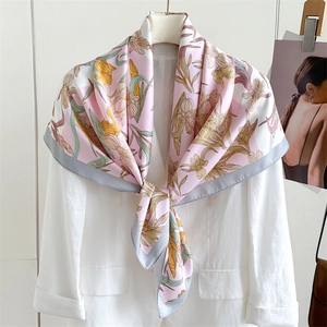 Carré en soie rose avec motifs floraux jaunes porté sur un blazer blanc élégant