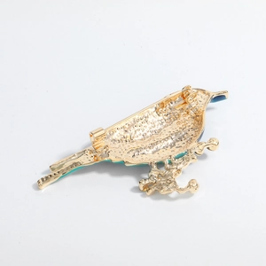 Minimalist bird brooch in gold alloy with blue-green enamel detail and safety pin back
