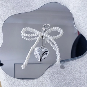 Detail of white faux pearl bow charm with silver heart pendant and heart-shaped lobster clasp
