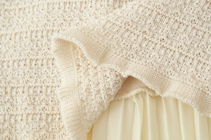 Gros plan détaillé sur la maille ajourée et l'ourlet plissé en ton beige crème doux