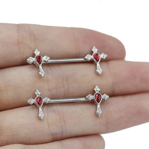 Macro shot of silver cross nipple rings with red teardrop stones on hand model