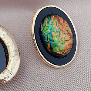 Macro shot of vintage gold earrings with textured edges and colorful foil inlay detail